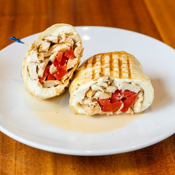 Grilled chicken and red pepper wrap, cut in half, on a white plate with a wooden background.
