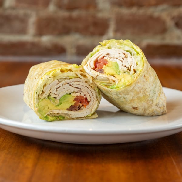 Two halves of a chicken and avocado wrap with lettuce and tomato on a white plate.
