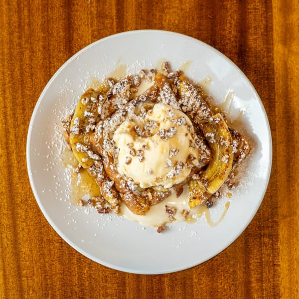 Caramelized bananas topped with vanilla ice cream, powdered sugar, and chopped nuts on a white plate.