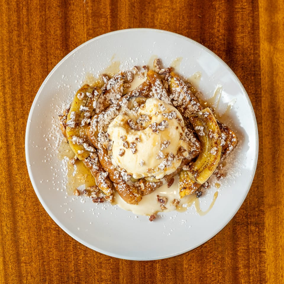 Caramelized bananas topped with vanilla ice cream, powdered sugar, and chopped nuts on a white plate.