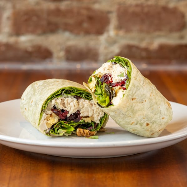 Two halves of a chicken salad wrap with lettuce, cranberries, and walnuts on a white plate.