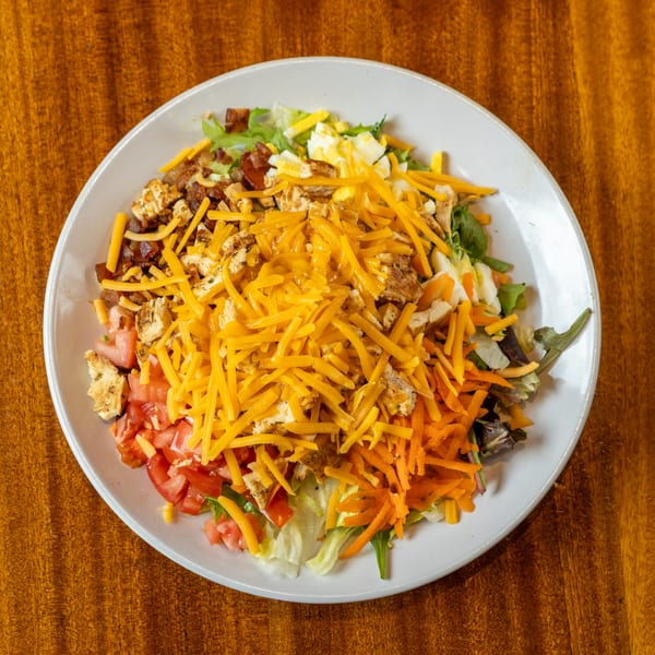 A vibrant salad with shredded cheese, chicken, tomatoes, carrots, and lettuce on a white plate.