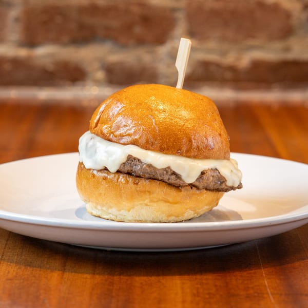 A single slider with melted white cheese and a wooden pick on a white plate.