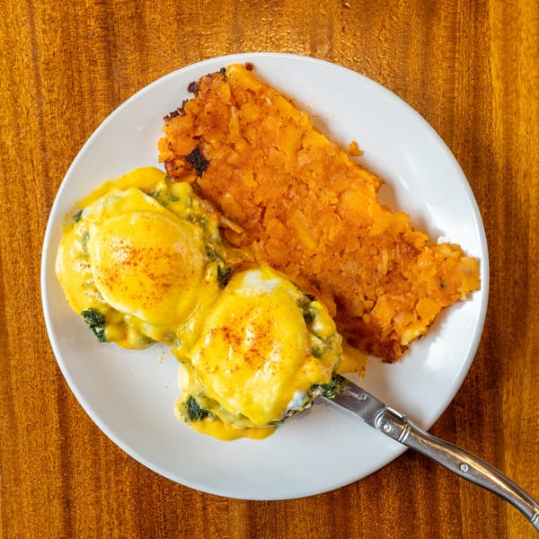 Eggs Benedict with hollandaise sauce and a side of crispy hash browns on a white plate.